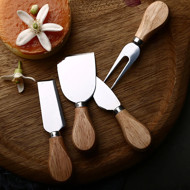 Set of four cheese knives with wooden handles on a wooden board with a small round cake and flowers.