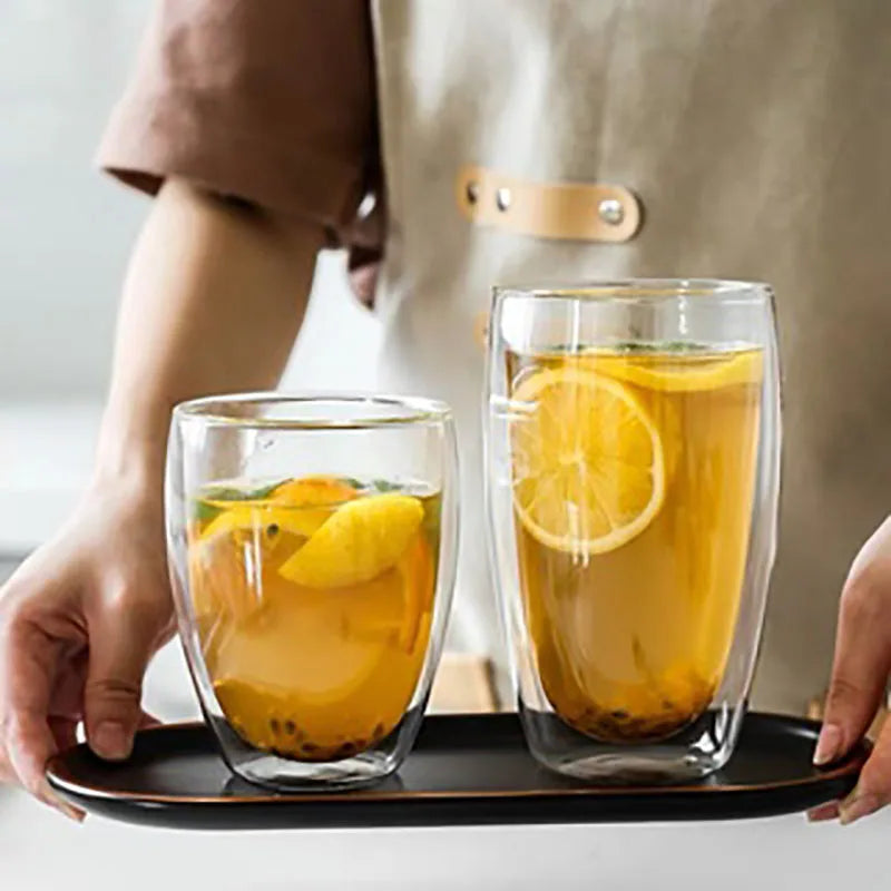 Two glass cups with lemon slices on a tray held by a person.