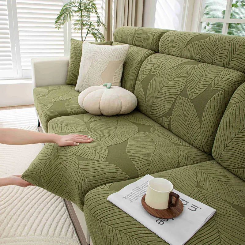 Green leaf-patterned sofa with a hand touching it, a cup on a saucer, and a plant in the background.