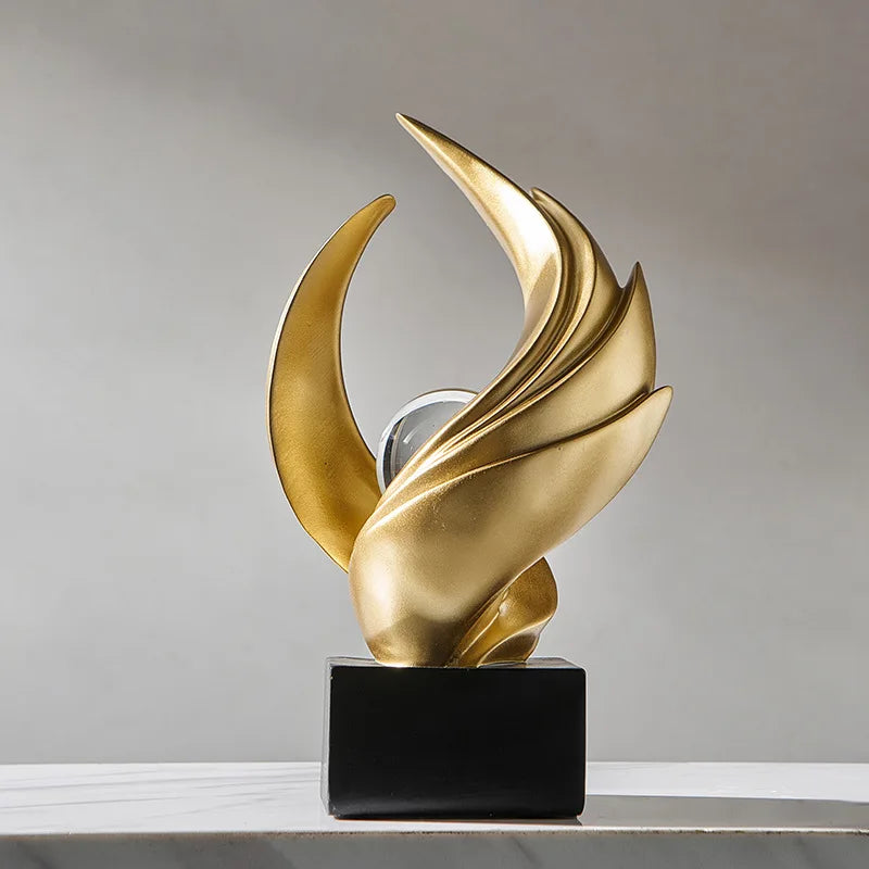 Gold abstract sculpture on a black base against a gray background