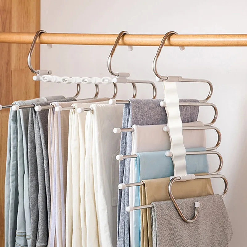 Multi-layered hanger with pants on a wooden rod against a neutral background