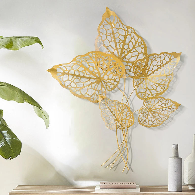 Decorative gold leaf wall art on a white wall with green leaves and a vase in the background.