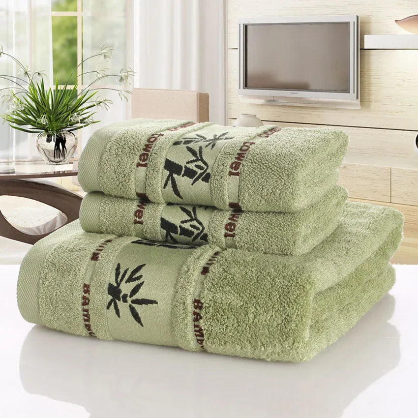 Set of green towels with bamboo design on a white surface, with a TV and plant in the background.