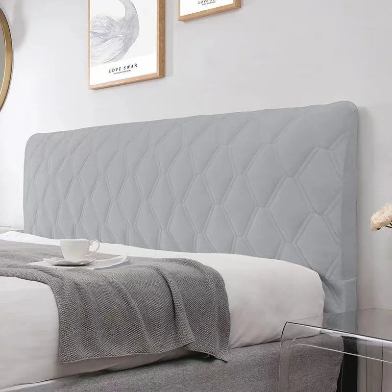 Gray quilted headboard on a bed with white bedding and gray blanket.