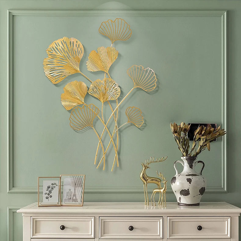 Decorative wall art with gold leaf design on a green wall above a white cabinet.