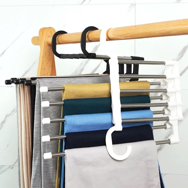 Multi-layered hanger with folded clothes on a wooden rod against a white tiled wall.