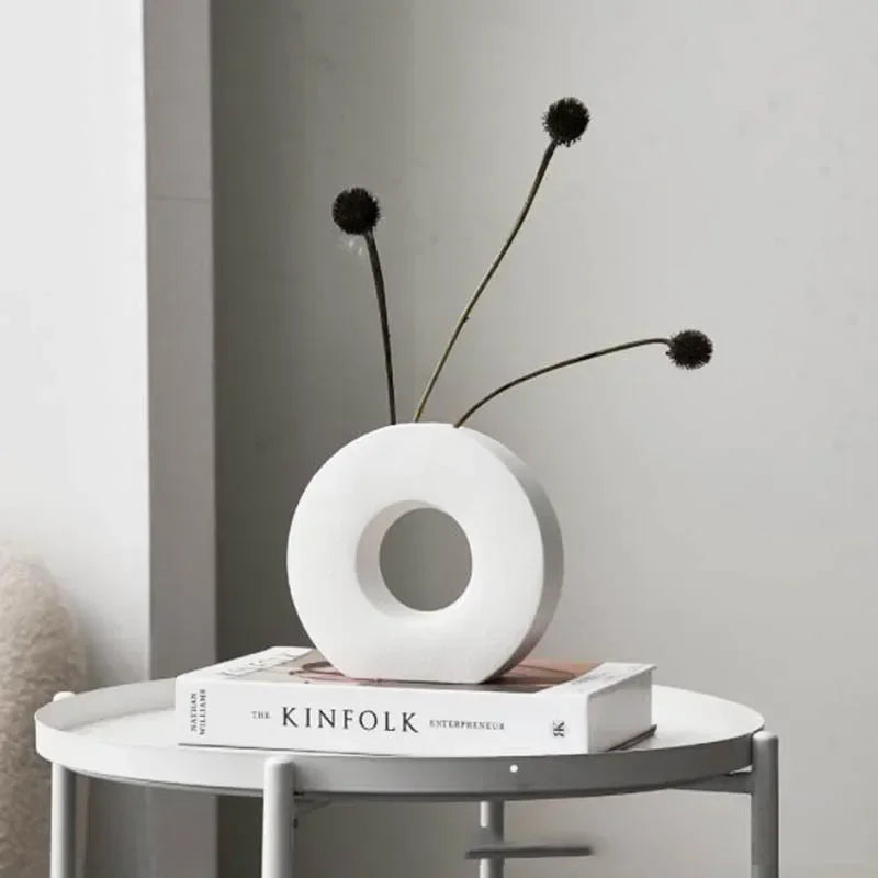 White vase with dried plants on a book titled 'KINFOLK' on a small round table.