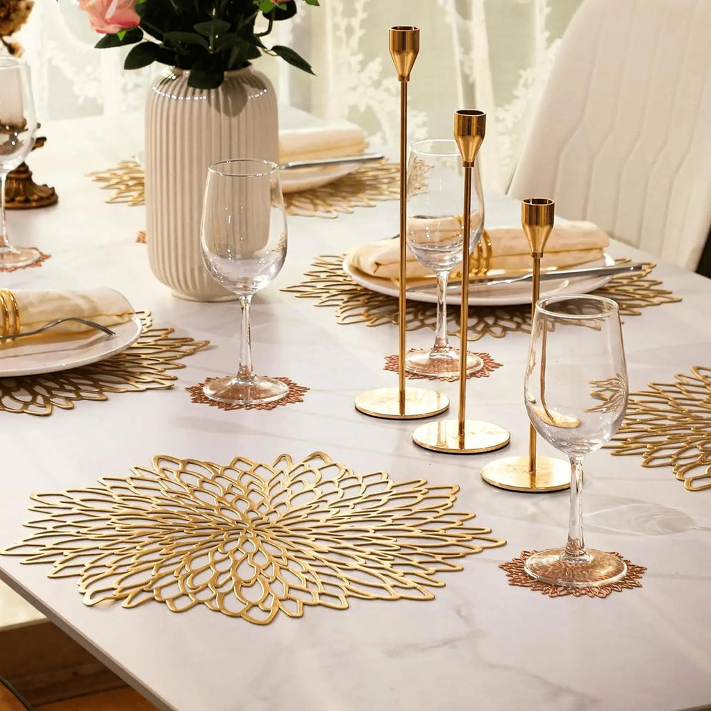 Elegant table setting with gold placemats, glasses, and candle holders on a white tablecloth.