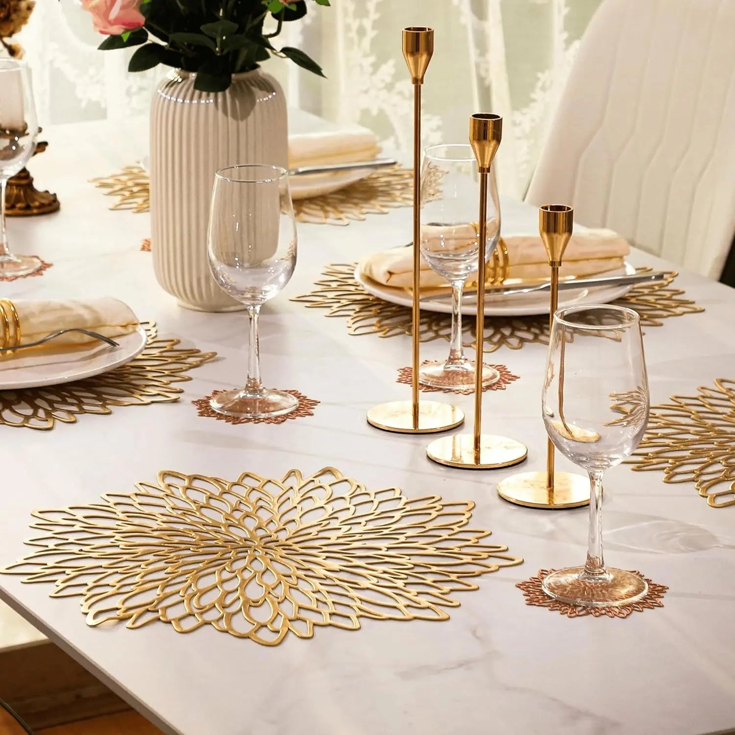 Elegant table setting with gold placemats, glasses, and candle holders on a white tablecloth.
