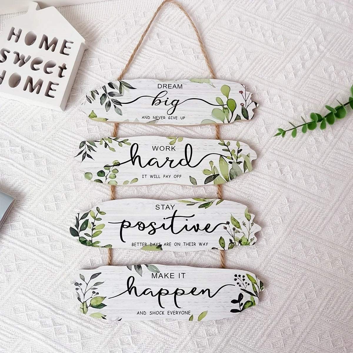 Decorative wall art with motivational phrases and greenery on a textured white background