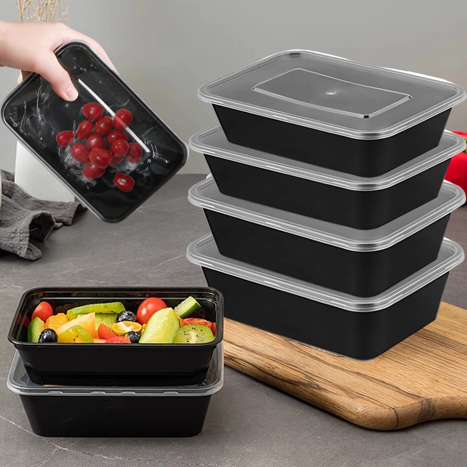 Set of black food containers with clear lids on a gray surface, one container is opened with fruits.