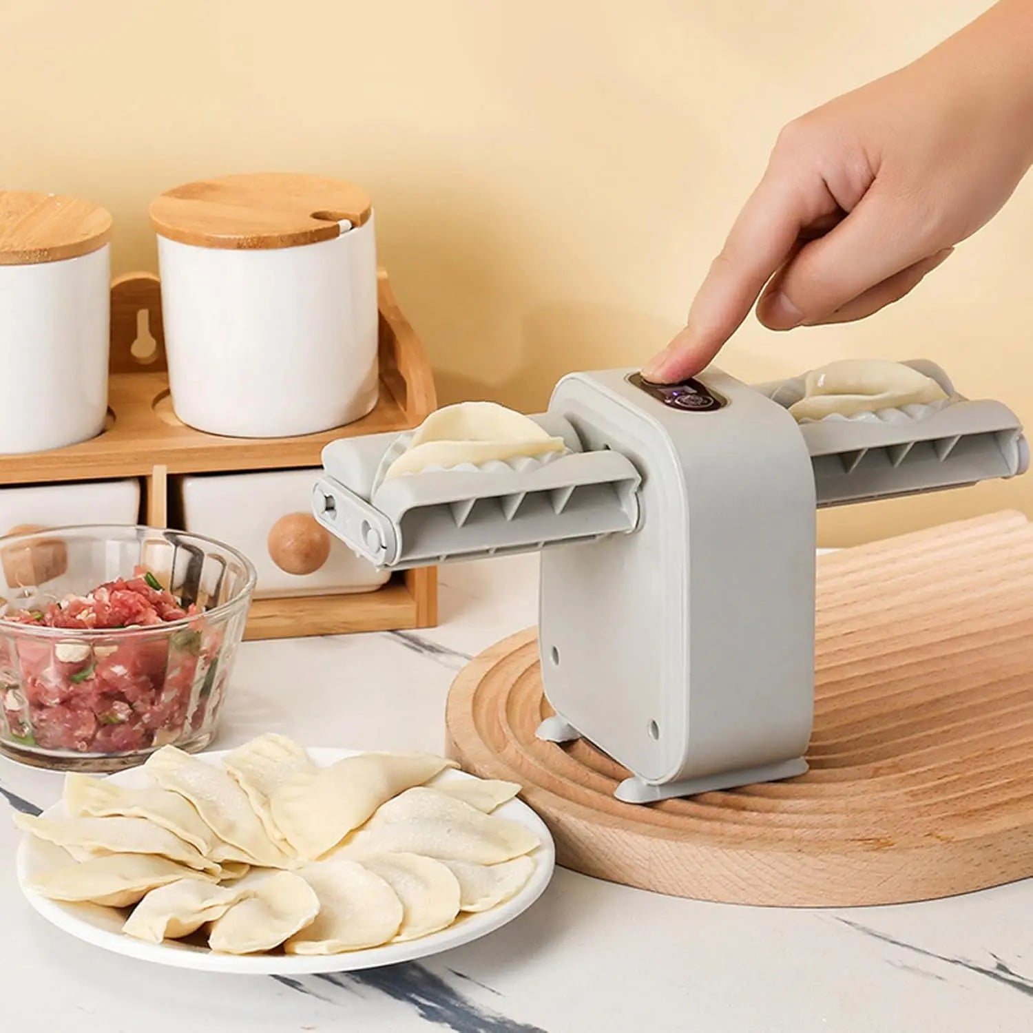 Hand using a dumpling maker with pre-made dumplings on a plate, kitchen setting.