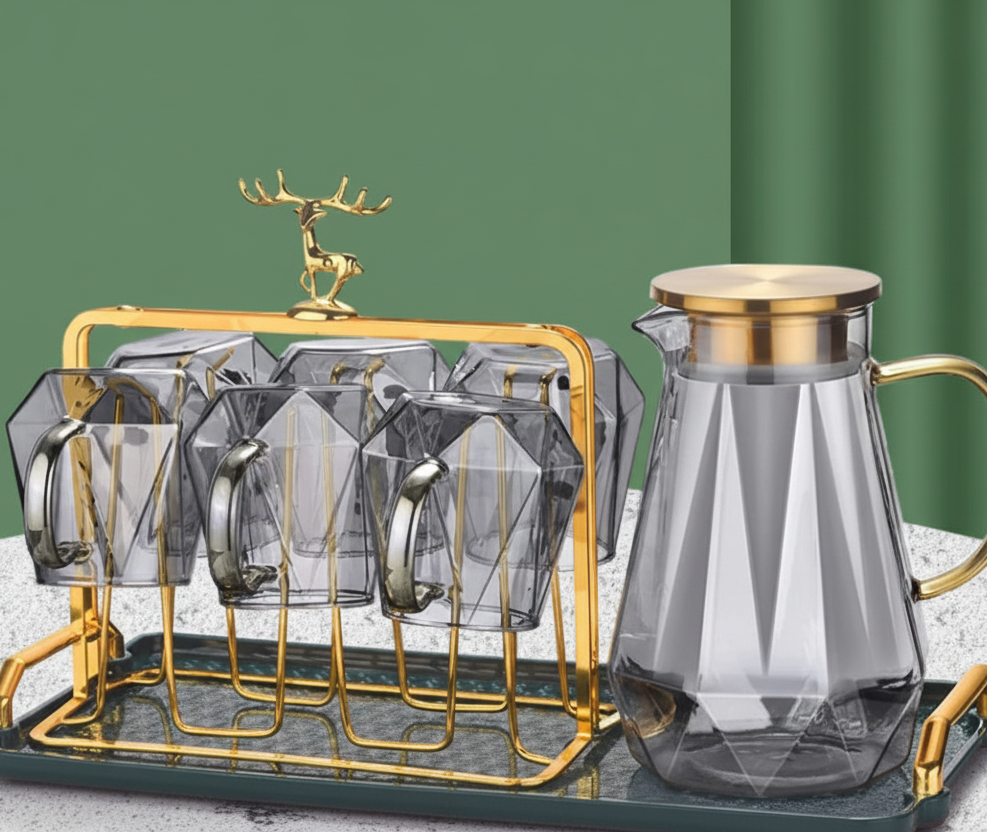 Glass cups with gold stands and a glass carafe on a marble surface with a green background.