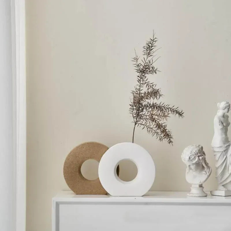 Decorative items including a white vase with branches, cork roll, and small statues on a shelf against a beige wall.