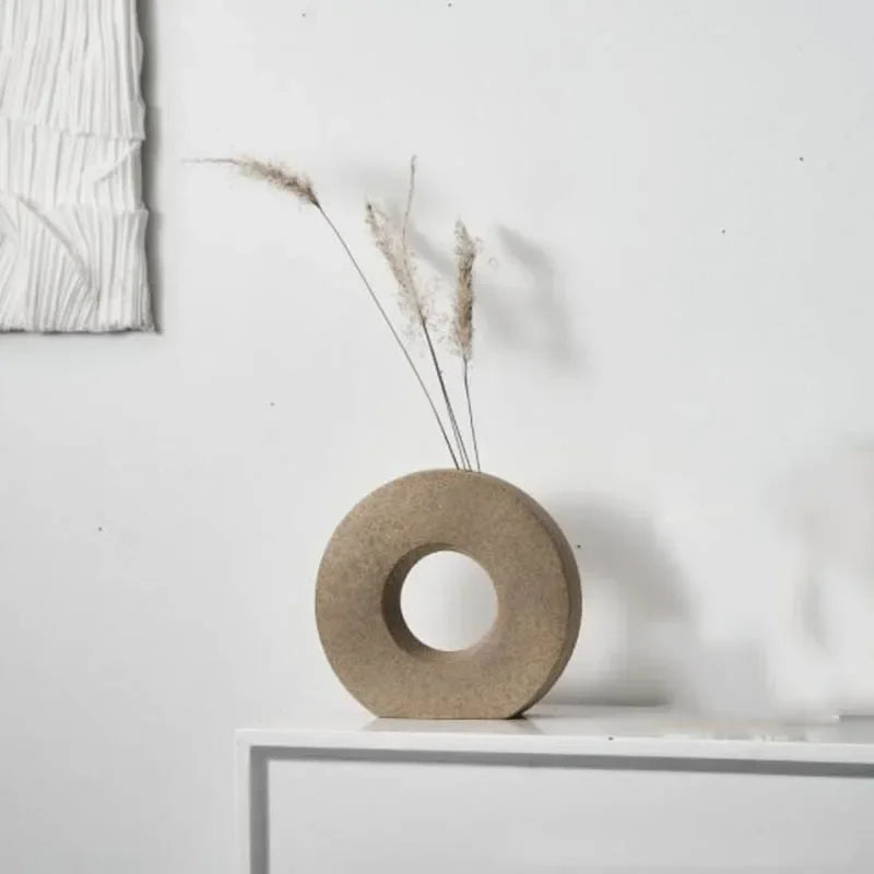 Decorative stone vase with a circular design on a white surface against a light gray wall.