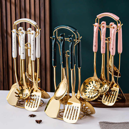 Set of gold kitchen utensils on a white surface with a dark green wall in the background.