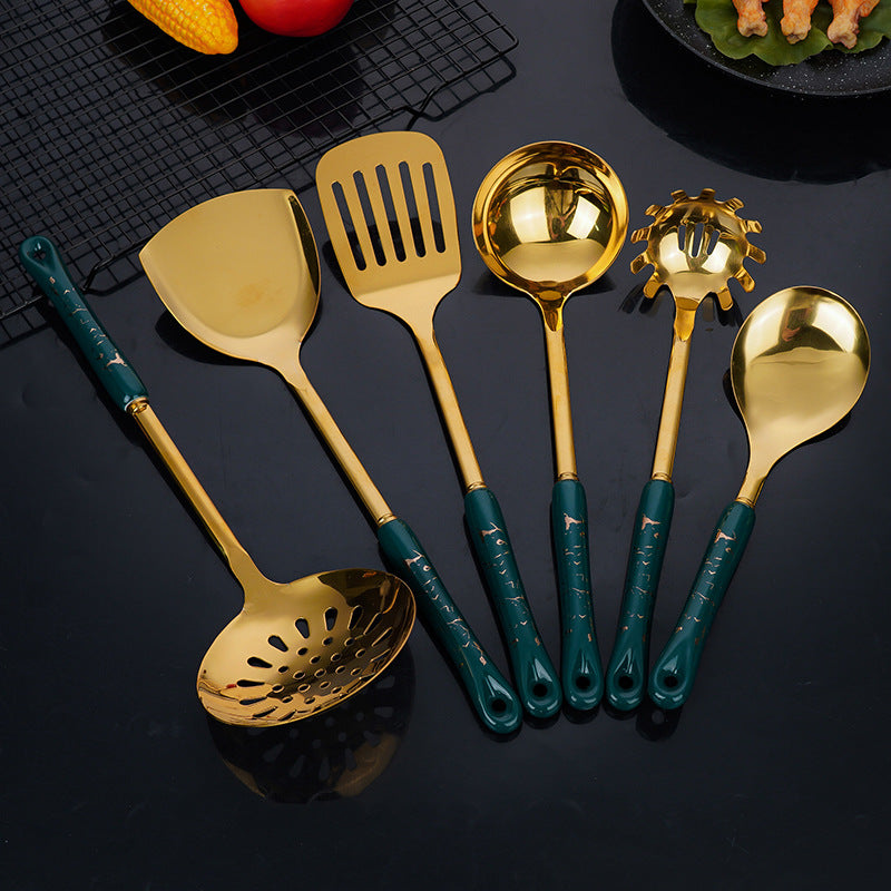 Set of gold kitchen utensils with green handles on a black surface