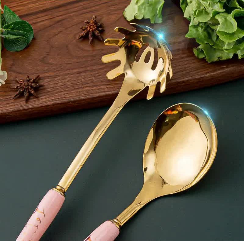 Gold spoon with pink handle on a dark surface with greenery