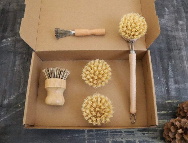 Set of natural cleaning brushes in a cardboard box on a dark textured surface.
